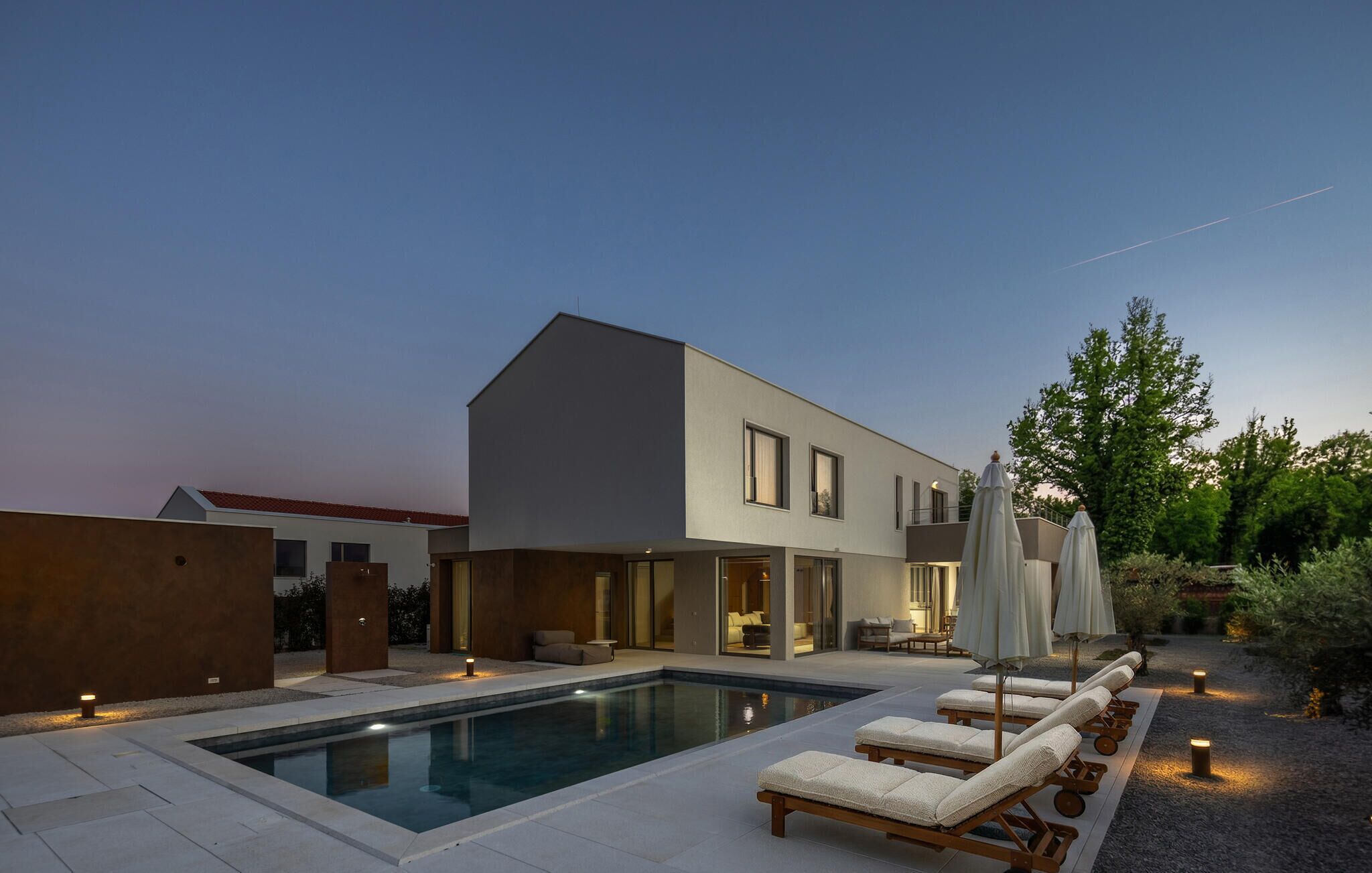 Ein modernes Haus mit Schwimmbad, Liegestühlen und Außenbeleuchtung.