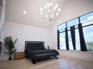 Ein modernes Schlafzimmer mit einem Bett, einer Zimmerpflanze, einem Nachttisch und einem großen Fenster mit Vorhängen.