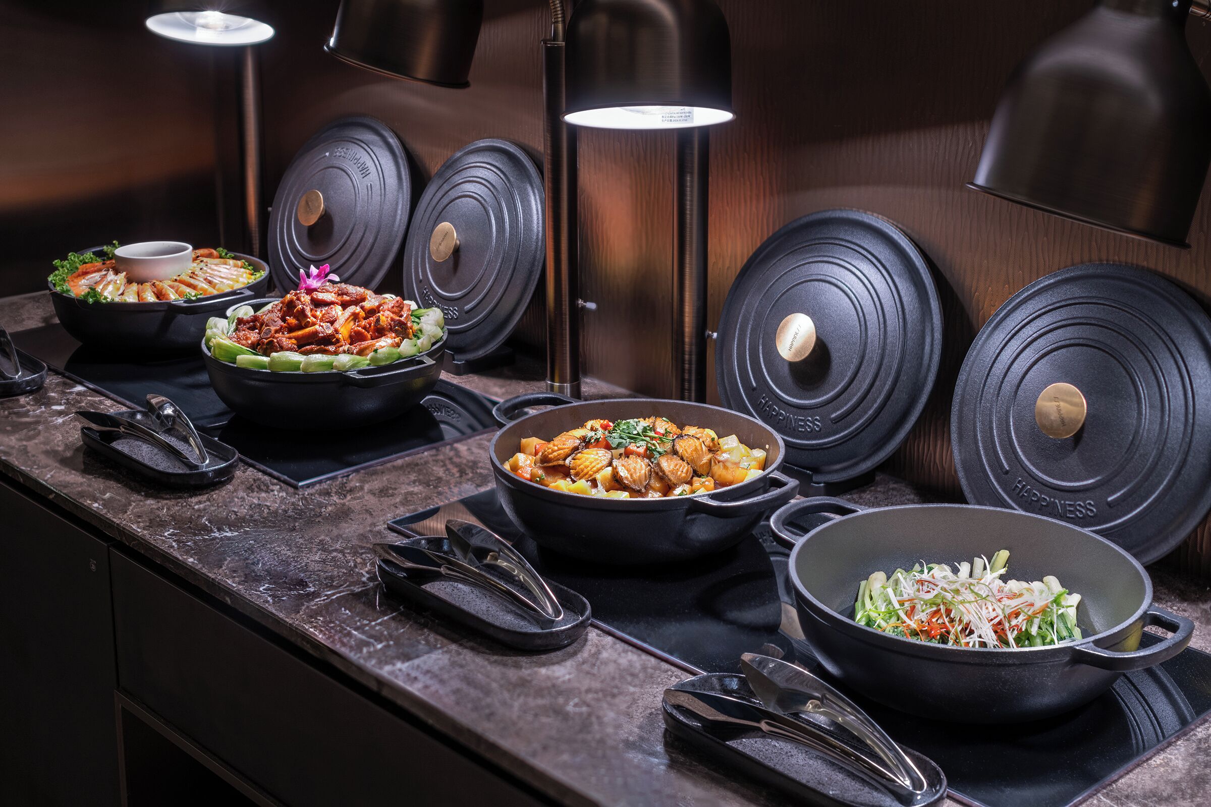 Een buffetopstelling met diverse gerechten, zwarte serveerschaaltjes en een moderne keuken op de achtergrond.