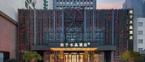 A hotel entrance with a modern facade, illuminated signage, and a geometric glass structure.