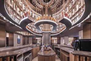 A modern bar area with a central circular light fixture, multiple shelves with bottles, and a bar counter. - Crystal Hotel qingdao wusi plaza haijing (Qingdao)