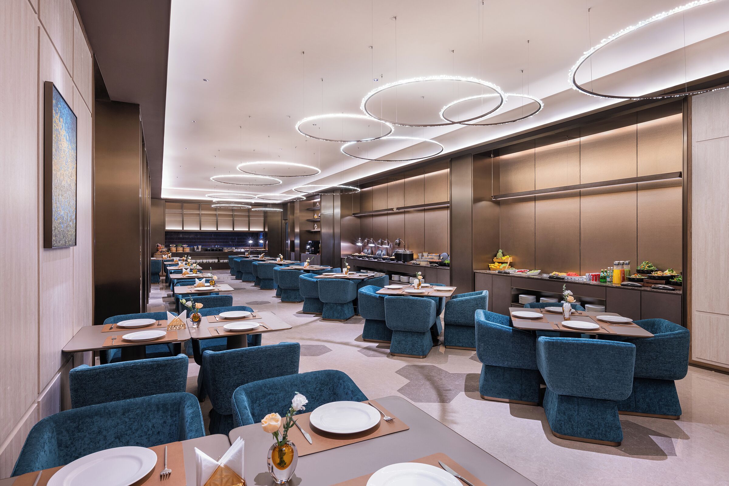 Un restaurante moderno con sillas tapizadas en azul, mesas redondas y una zona de cocina central.