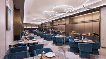 A modern restaurant with blue upholstered chairs, round tables, and a central kitchen area.