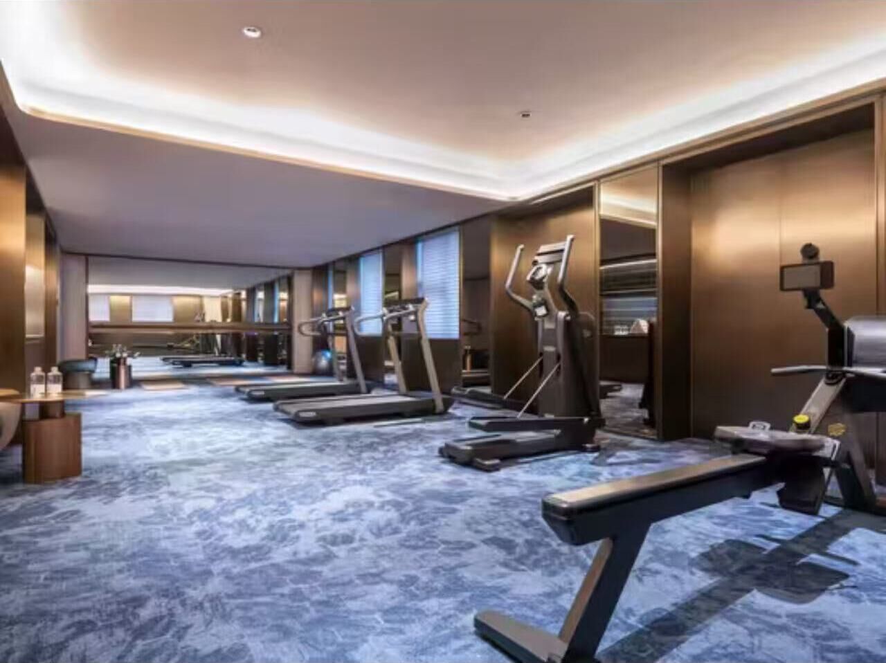 A hotel fitness center with treadmills, stationary bikes, and a mirrored wall.