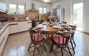 Eine Küche mit Esstisch für vier Personen, einem Kühlschrank und einem Fenster mit Blick auf einen Garten.