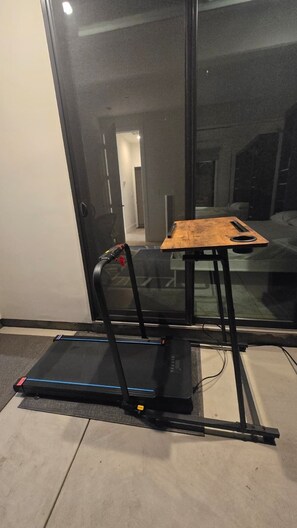 Ein Laufband in einem Zimmer mit großem Fenster, einer Tür und Teppichboden.