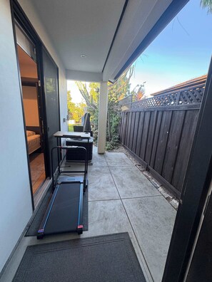 Une terrasse couverte équipée d’un tapis de course, d’une table et de chaises, d’une clôture en bois et d’une porte donnant sur une pièce.