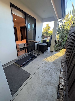 A modern outdoor space with a sliding glass door leading to a bedroom, a treadmill, and a patio area with a chair and table.