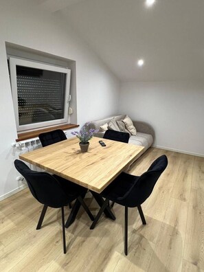 Ein Essbereich mit Holztisch, schwarzen Stühlen, einer Zimmerpflanze und einer Couch.