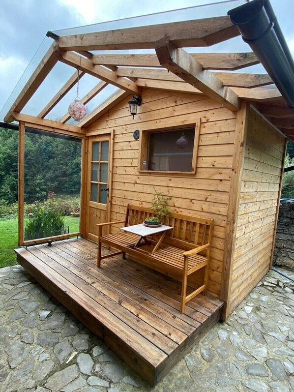 Eine Holzhütte mit Veranda, einer Bank, einem Tisch und einem Fenster.
