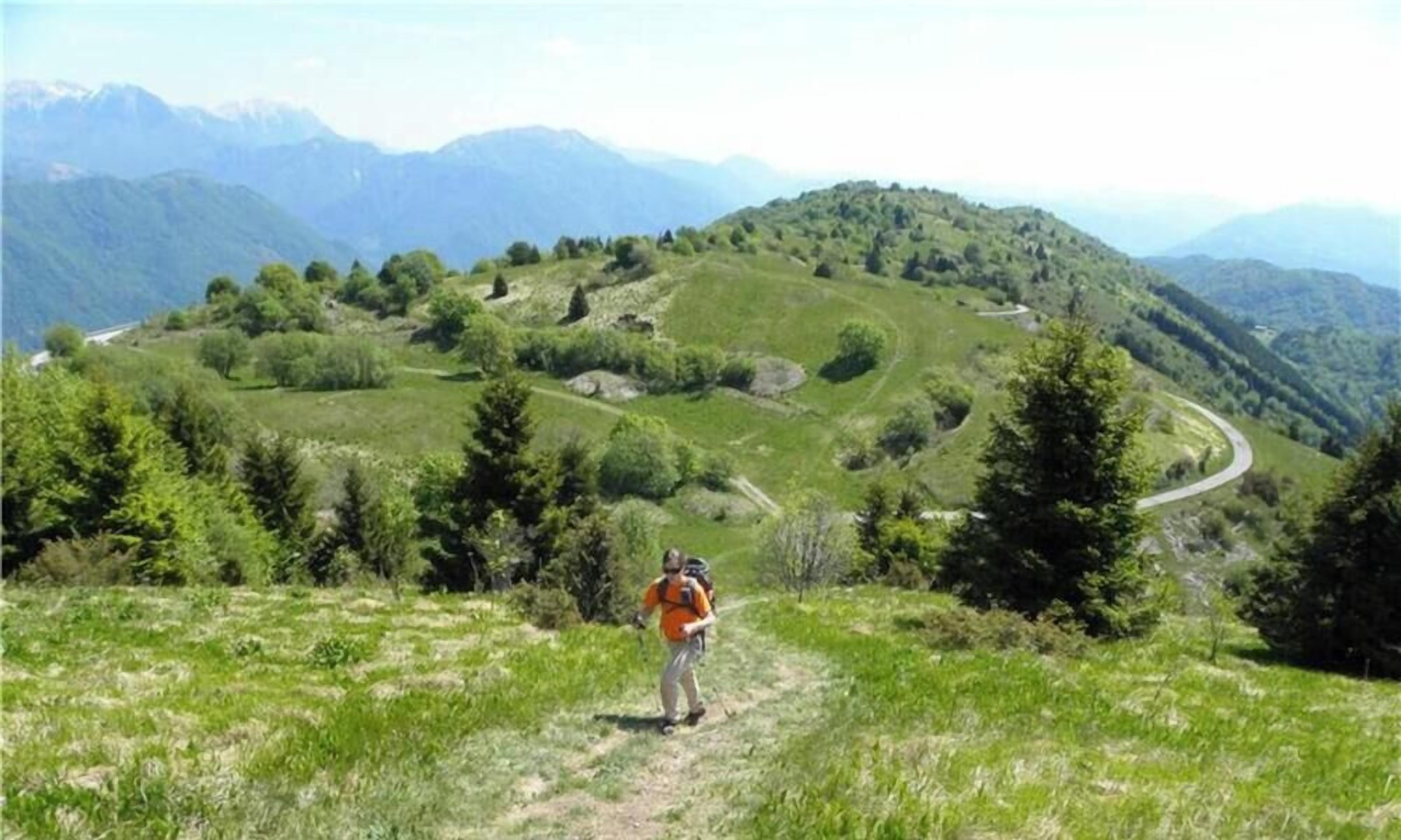 Un randonneur sur un sentier herbeux, avec des montagnes en arrière-plan.