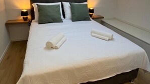Een slaapkamer met dakraam, een bed met witte lakens, twee kussens en twee bedlampjes.