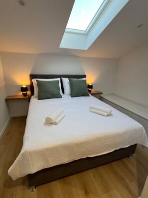 Ein Schlafzimmer mit Oberlicht, einem Bett mit weißen Leinen, zwei Kissen und zwei Nachttischlampen.