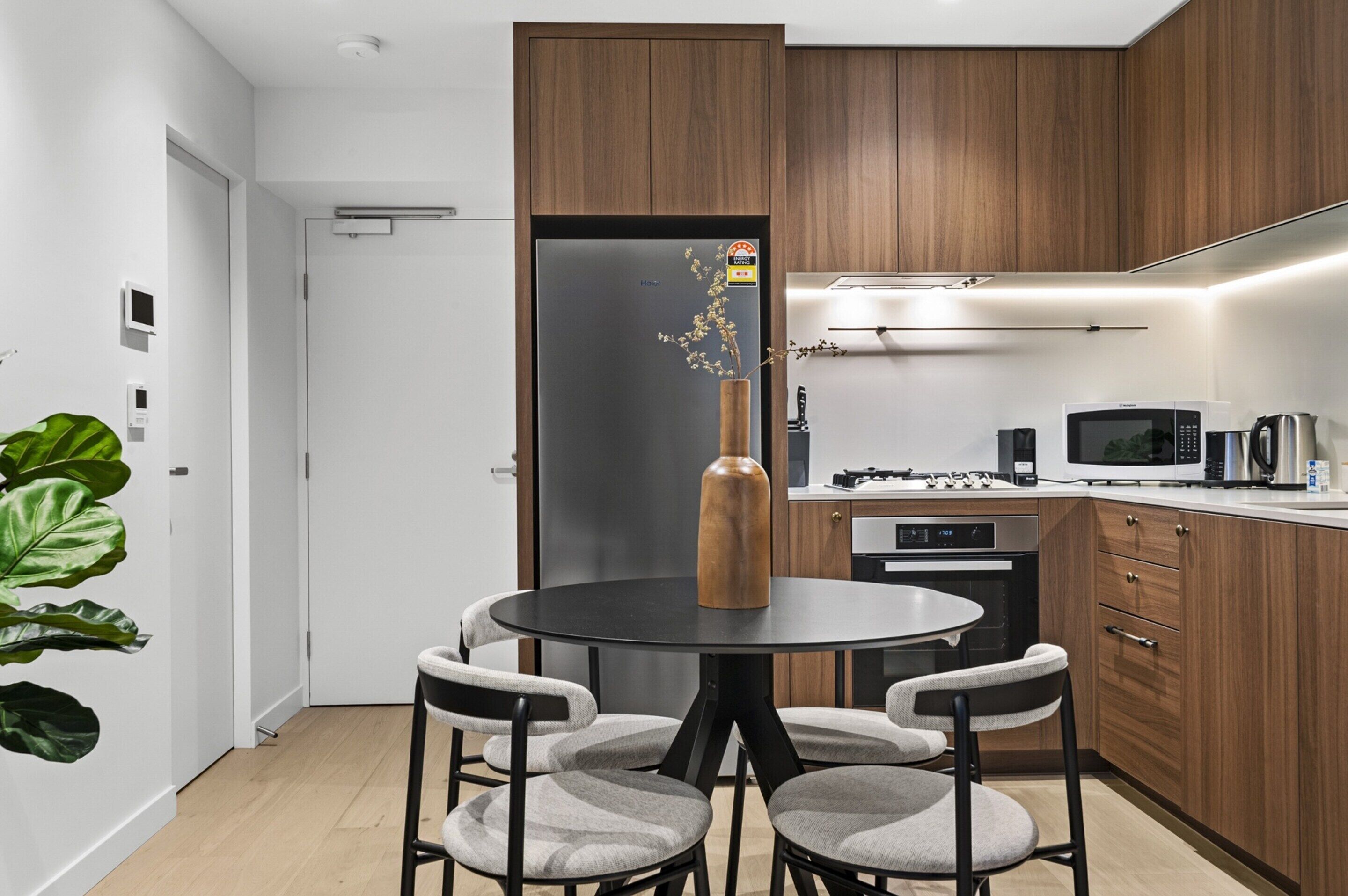 Une cuisine moderne avec des meubles en bois, un réfrigérateur noir, une table à manger avec quatre chaises et une machine à café.