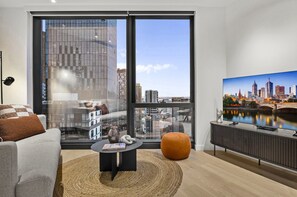 Ein modernes Wohnzimmer mit großem Fenster, einer Couch, einem Couchtisch und einem Fernseher.