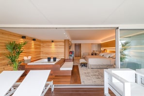 Una habitació d'hotel moderna amb interior de fusta, un llit gran, zona de seients amb sofà i taula, i una porta de vidre que dona a un balcó.