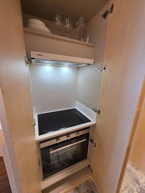 Una cocina compacta con horno integrado, microondas y una estantería con copas de vino.