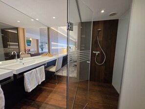 Un baño moderno con cabina de ducha de vidrio, tocador doble y suelo de madera.