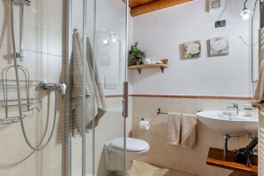 Kylpyhuone, jossa on lasiseinäinen suihkukaappi, wc, pesuallas ja pyyheteline.