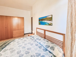 Quarto com cama, guarda-roupa de madeira e pintura de uma cena de praia.