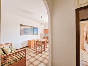 Une pièce confortable comprenant un lit, une table à manger avec des chaises, un coin cuisine et un grand tableau représentant une plage, accroché au mur.
