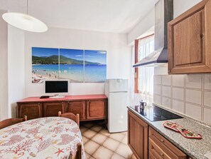 Una cocina con salpicadero de azulejos, armarios de madera, una encimera, un refrigerador y un comedor con mesa y sillas.