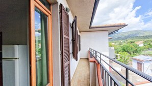 A balcony with a view of a mountainous landscape, a refrigerator, and wooden shutters on the windows. - Bilo C 4-bed Apartment with Balcony in Marina di Campo (Marina di Campo)