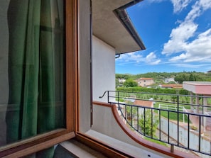 Un balcone con vista su una zona residenziale, una finestra con tenda e una ringhiera in metallo.