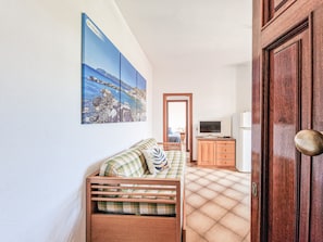 Una stanza con una panca in legno, un televisore su un mobiletto in legno e una porta con maniglia in ottone.