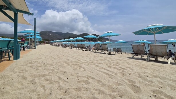 A beach with rows of sun loungers and umbrellas, a sandy beach, and a view of the sea and mountains in the background. - Bilo C 4-bed Apartment with Balcony in Marina di Campo (Marina di Campo)