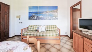 A room with a bed, a sofa bed, a television, and a painting of a coastal scene. - Bilo C 4-bed Apartment with Balcony in Marina di Campo (Marina di Campo)