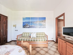 Una stanza con un letto, un divano letto, una televisione e un quadro raffigurante una costa.