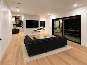 Ein modernes Wohnzimmer mit einer schwarzen Couch, einem Flachbildfernseher und einem Essbereich mit Tisch und Stühlen.
