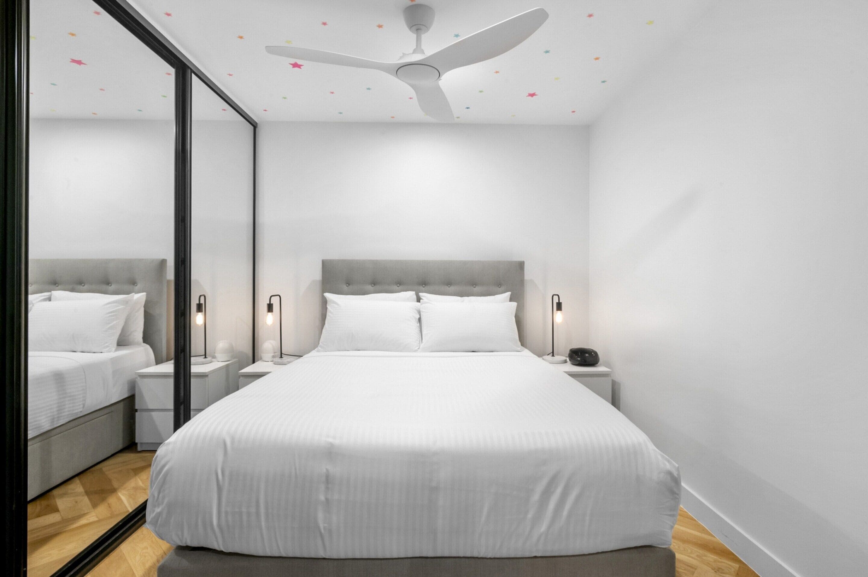 Un dormitorio con una cama grande, mesitas de noche, un ventilador de techo y un espejo.