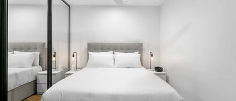 Un dormitorio con una cama grande, mesitas de noche, un ventilador de techo y un espejo.