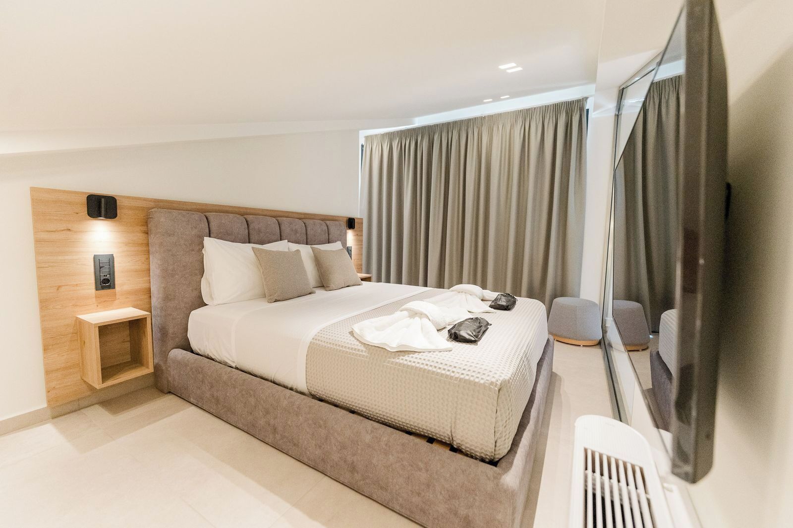 Un dormitorio moderno con una cama grande, cabecera de madera, mesita de noche, espejo y vistas al exterior.
