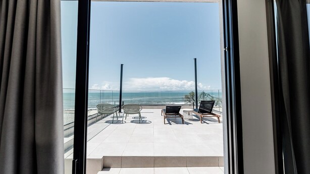Un balcón con dos sillas y una mesa, con vista a la playa y el océano.