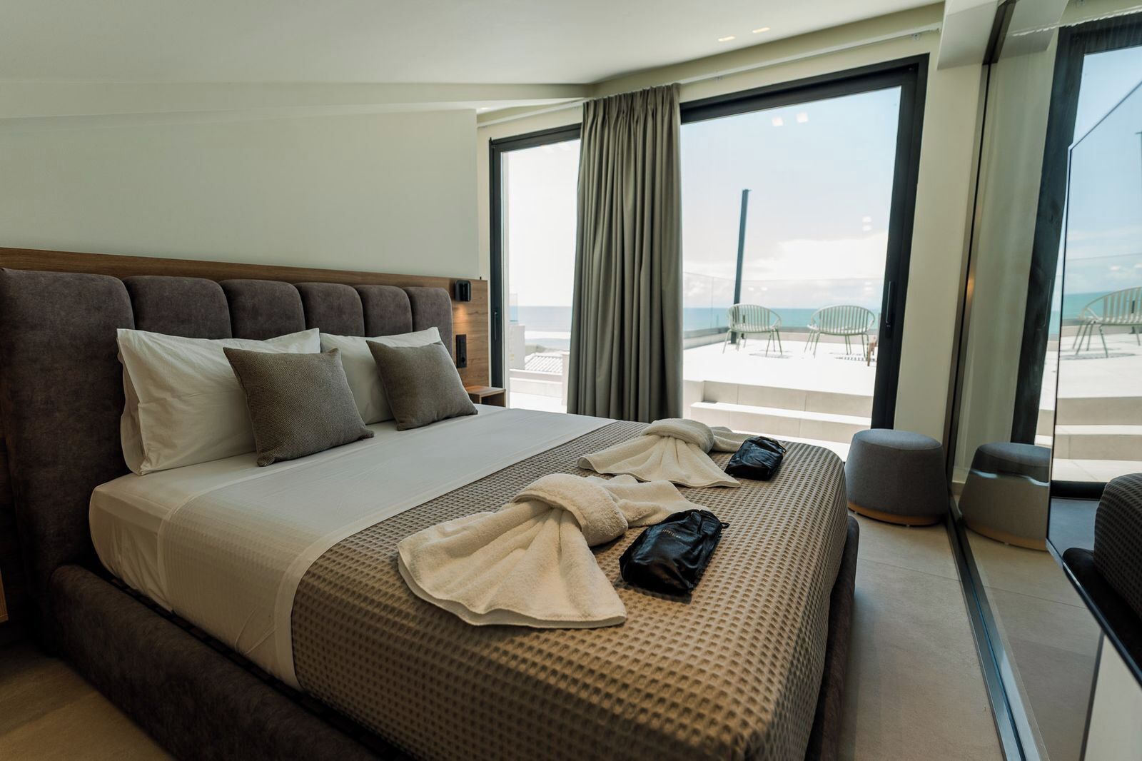 Ein Hotelzimmer mit einem großen Bett, Meerblick und einem Balkon mit Sitzgelegenheit.