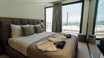 Ein Hotelzimmer mit einem großen Bett, Meerblick und einem Balkon mit Sitzgelegenheit.