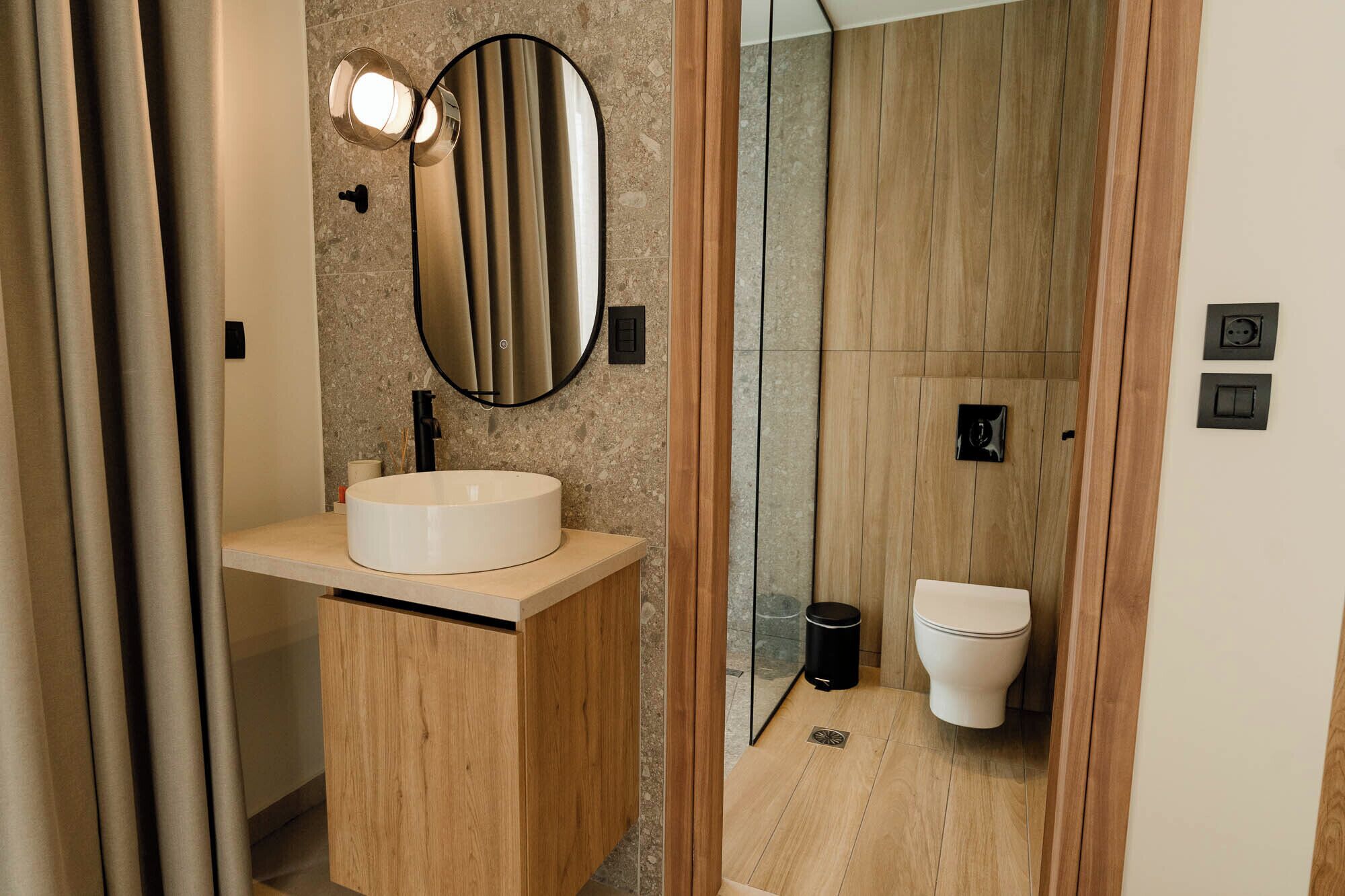 Un bany modern amb un vàter rodó, un mirall, un vàter i una cabina de dutxa de vidre.