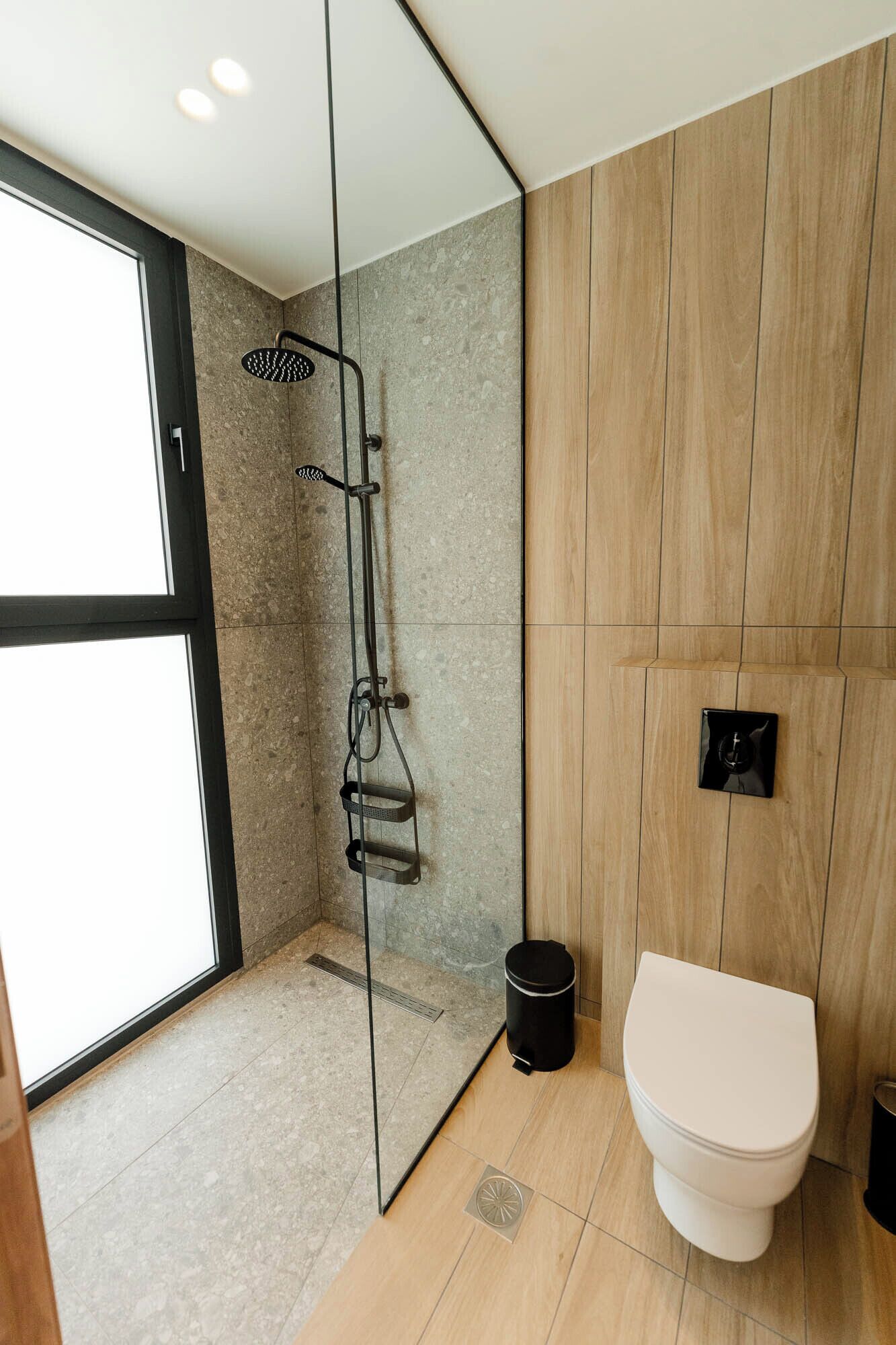 Un baño moderno con cabina de ducha de vidrio, inodoro y panel de pared de madera.