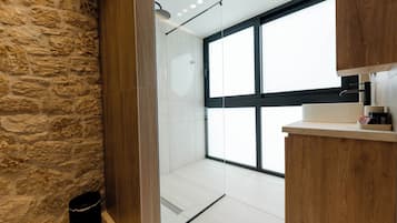 Un baño moderno con pared de piedra, cabina de ducha de vidrio y tocador de madera.