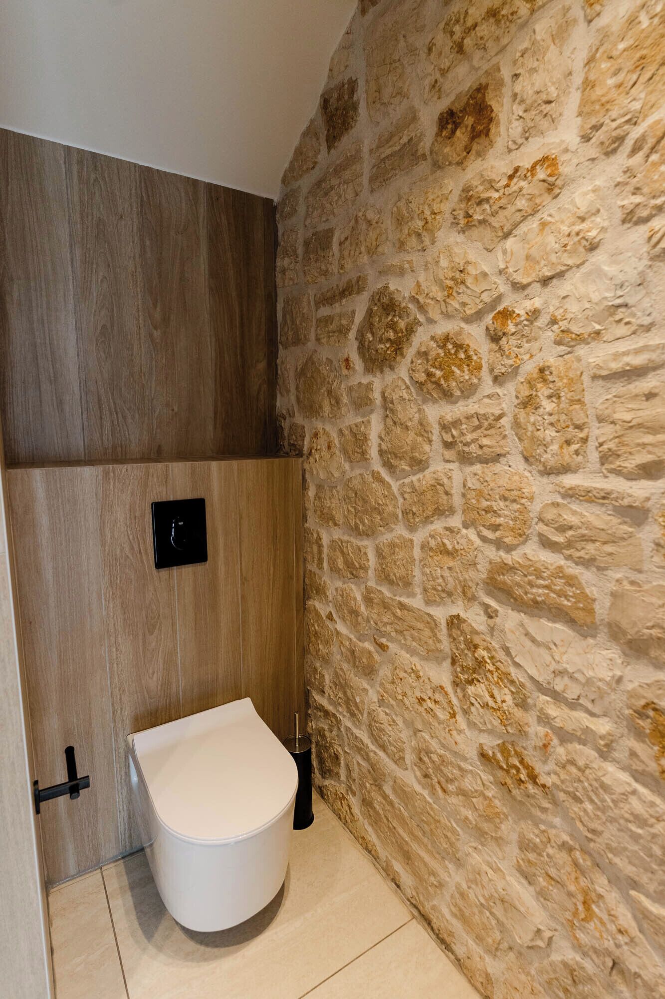 A bathroom with a stone wall, a wooden panel, and a white toilet.