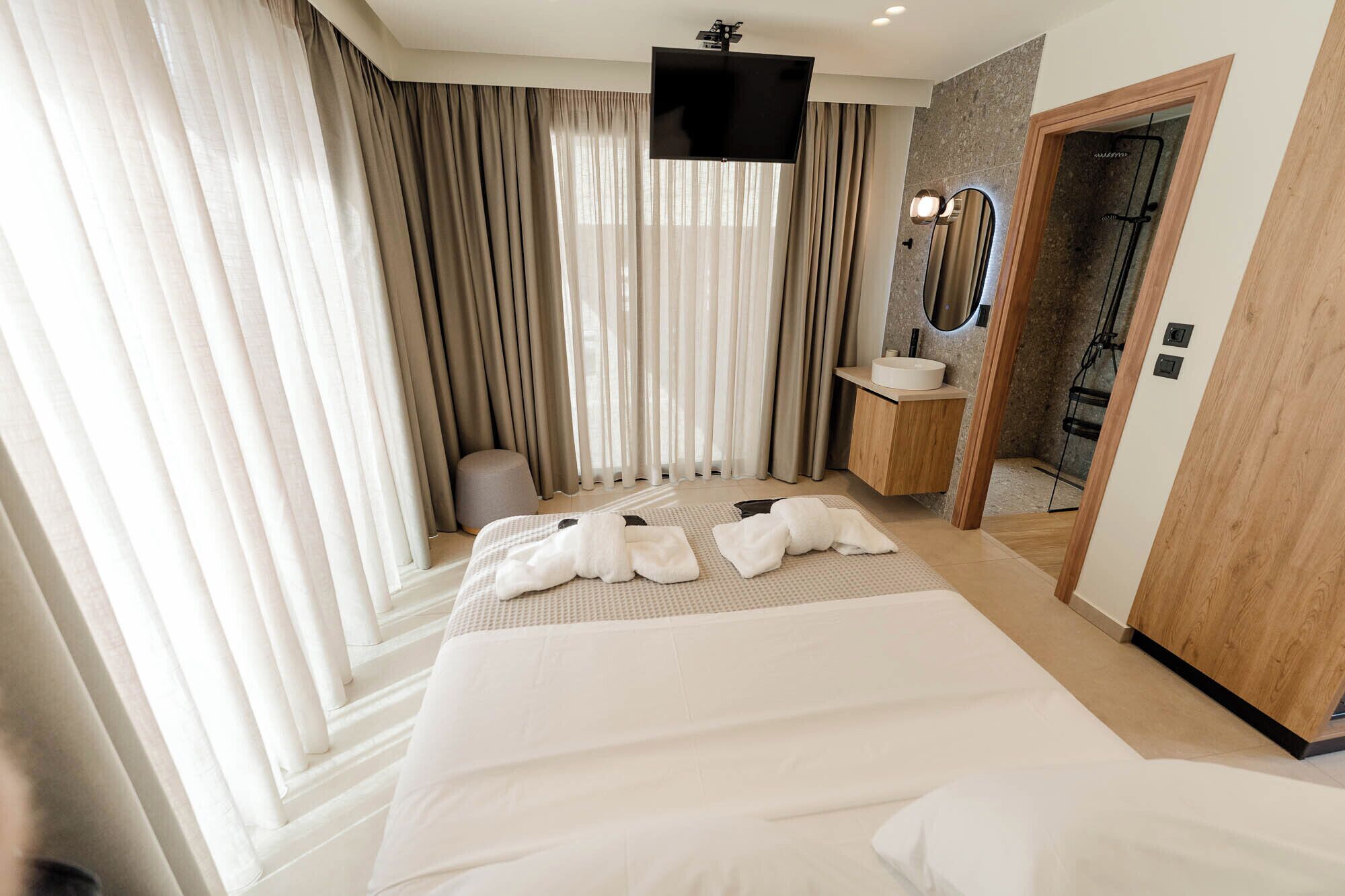 A hotel room with a large bed, a TV, a bathroom with a mirror, and a shower.