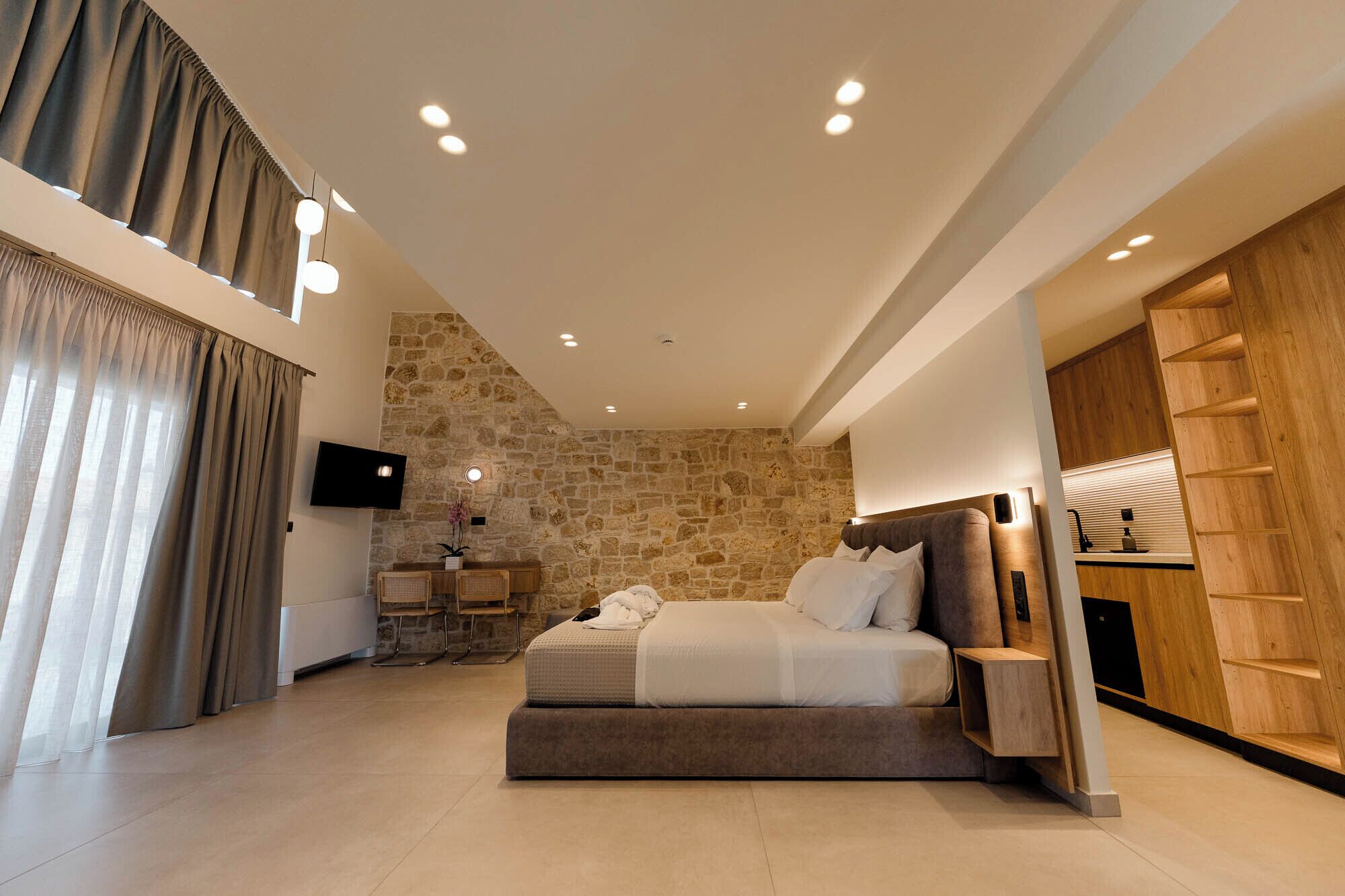 A modern bedroom with a stone accent wall, a bed, a TV, and a wooden wardrobe.