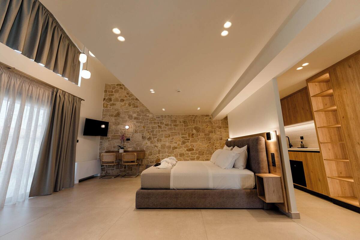 A modern bedroom with a stone accent wall, a bed, a TV, and a wooden wardrobe.