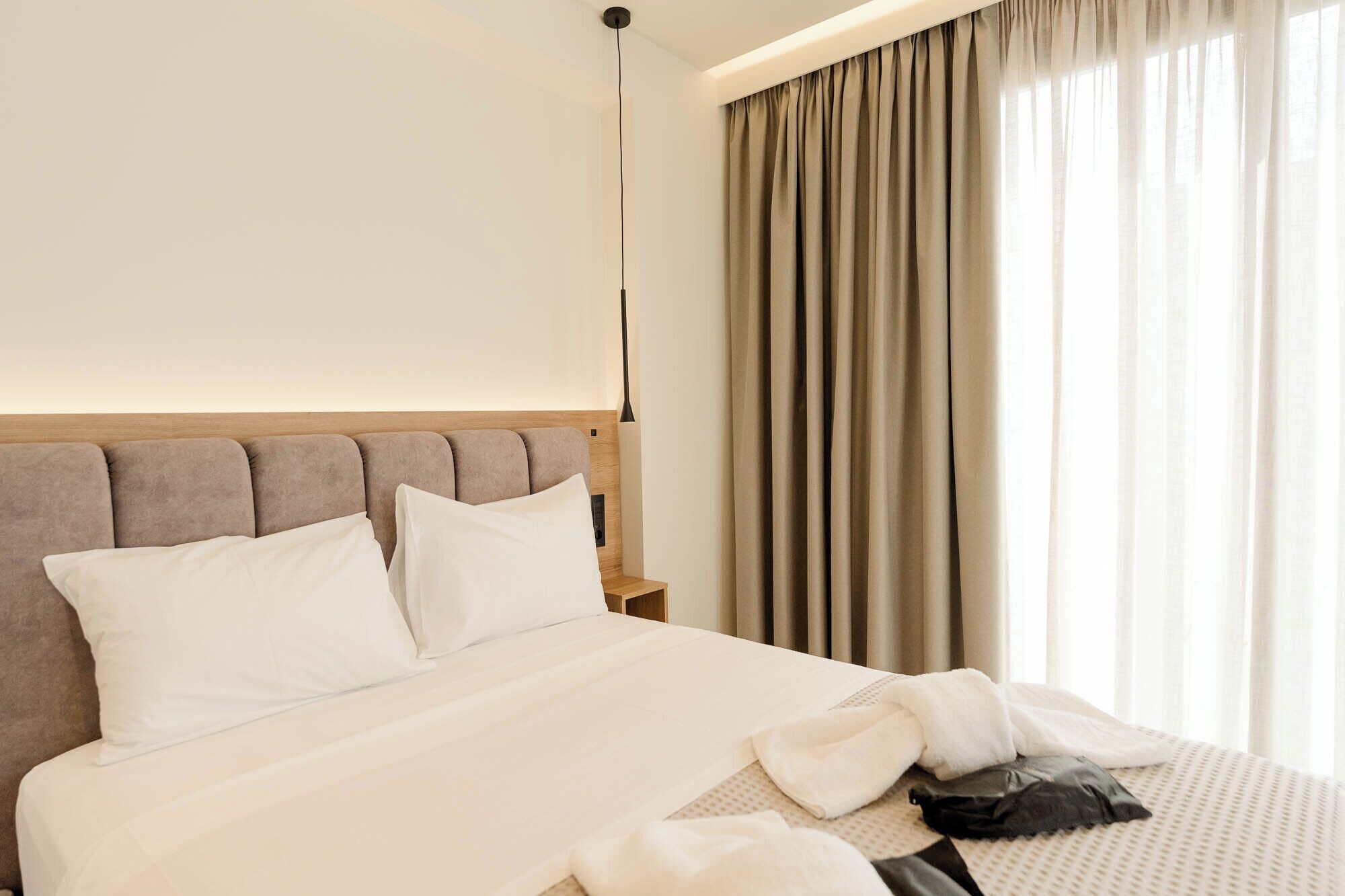 A hotel room with a bed, a nightstand, a lamp, and a window with curtains.