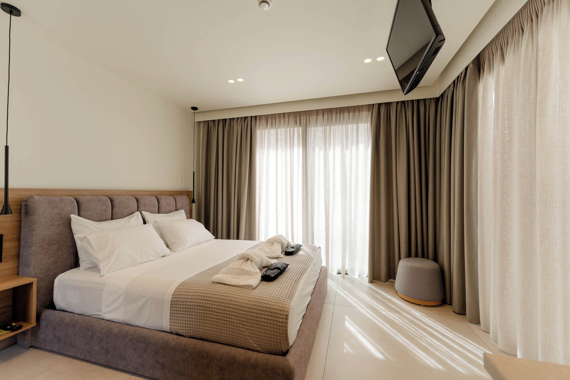 A modern hotel room with a large bed, a flat-screen TV, and a bedside table.