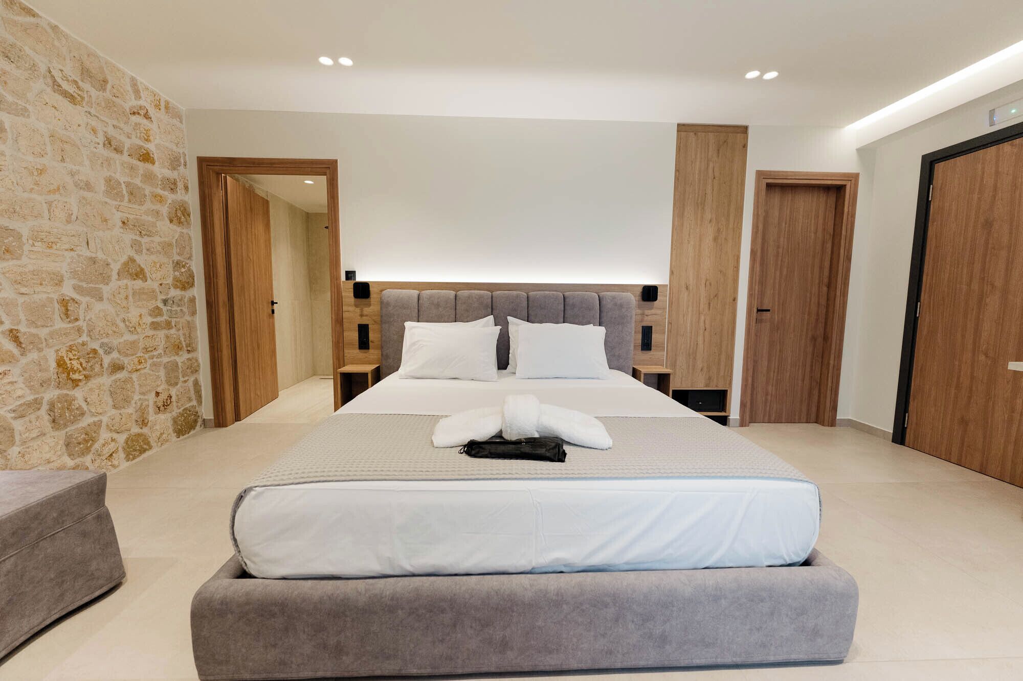 Un dormitorio moderno con una cama grande, una pared de piedra y puertas de madera.