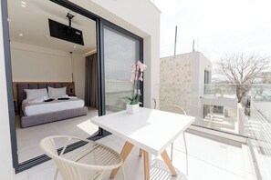 A modern bedroom with a bed, a bedside table, and a window. - Aetheria North (Amaliada)